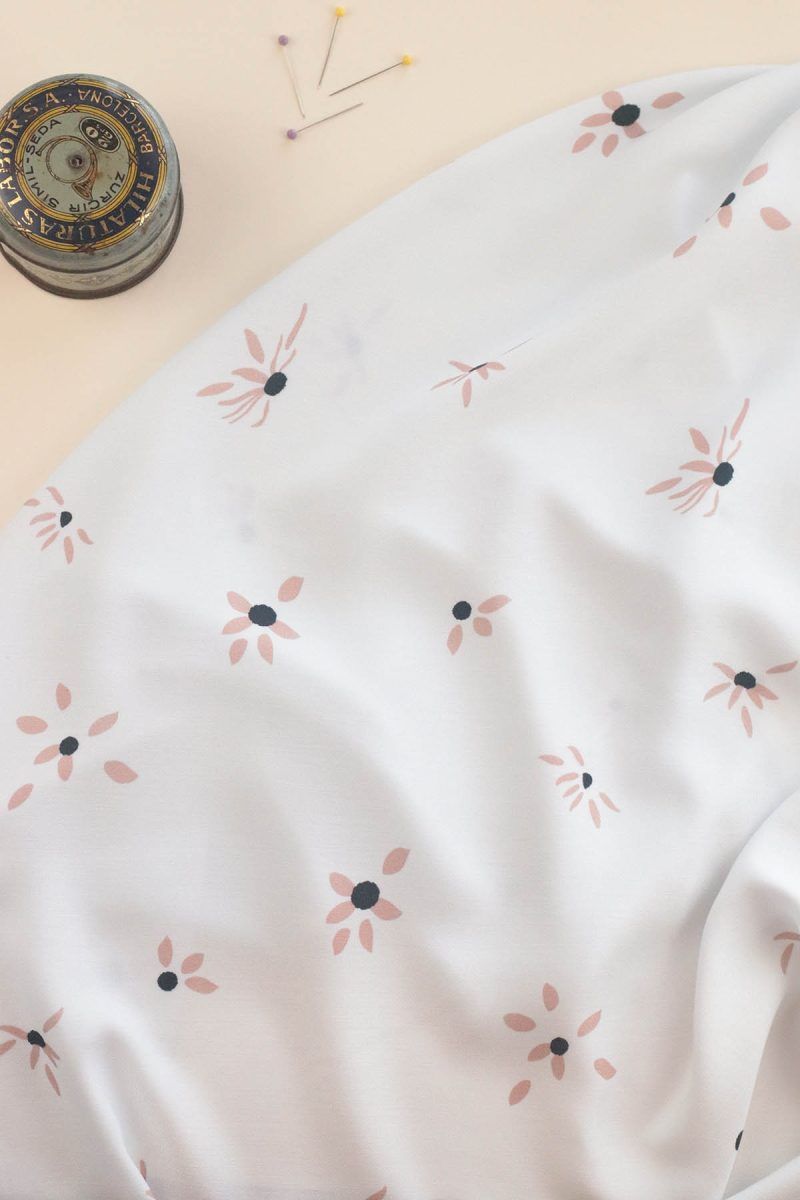 Tela de ecoviscosa color blanco roto con flores margaritas de color rosa y a las que se le están cayendo algunos pétalos