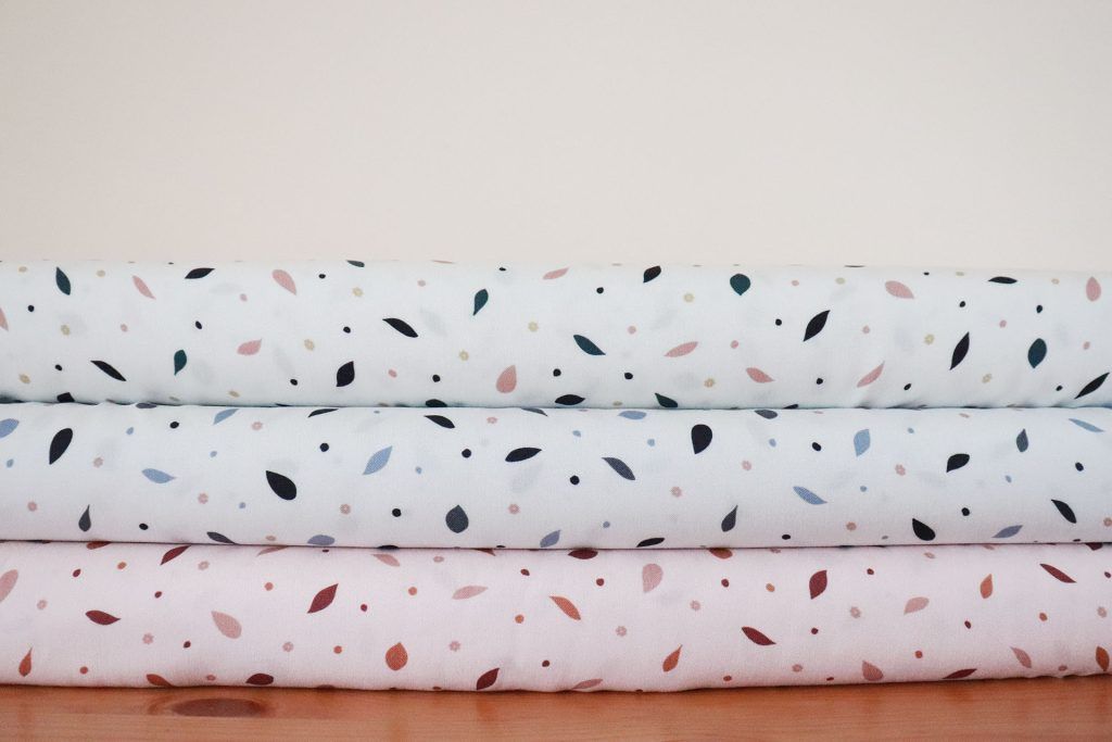 Tres tablillas de telas apiladas una encima de otra con estampados de pequeñas hojas rosas, azules y marrones.
