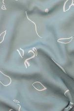 Detalle de tela de viscosa ODALOA con fondo verde con motivos de caras pictóricas, hojas y líneas simulando el viento en color blanco roto y crema