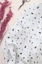 Tejido de ecoviscosa de fondo blanco roto con hojas en diferentes tonos de azul y pequeñas florecitas rosas.