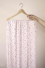 Viscosa EcoVero hojas rosa Una mano sujeta una percha de madera de la que cuelga una larga tela de color rosa con motivos de pequeñas hojas en colores ciruela, rosa oscuro y marrón.