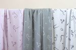Tres largas telas de viscosa en colores verde grisáceo, malva y blanco roto cuelgan de una barra. Tienen motivos de caras abstractas y líneas de viento.