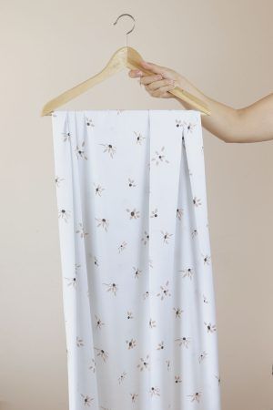 Una mano sujeta una percha de madera de la que cuelga una larga tela de color blanco con flores rosas.
