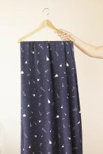 Una mano sujeta una percha de madera de la que cuelga una larga tela de color azul oscuro con flores y pétalos blancos y rosas.