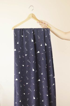 Una mano sujeta una percha de madera de la que cuelga una larga tela de color azul oscuro con flores y pétalos blancos y rosas.