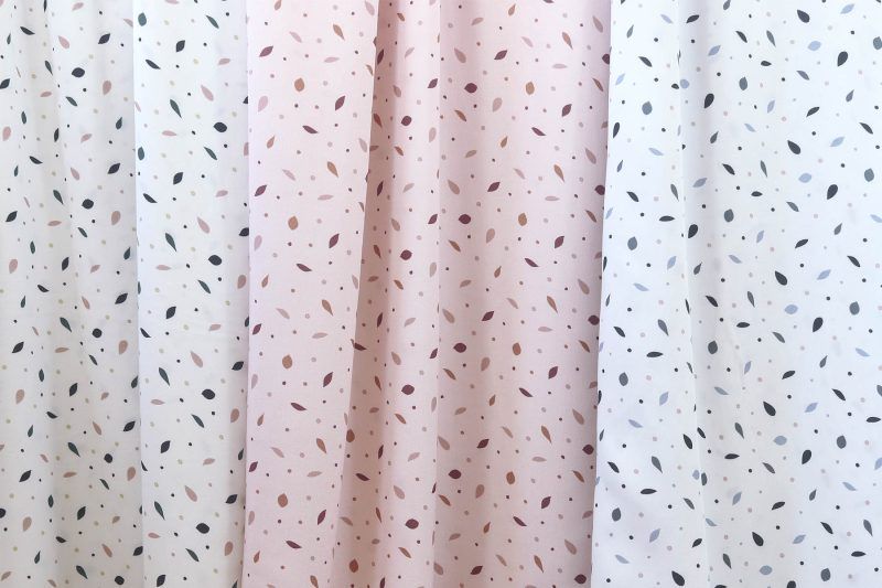 Tres largas telas que cuelgan, todas ellas con motivos de pequeñas hojas. Dos tienen fondo blanco, una con hojas azuladas y otra con hojas azules, verdes y rosas, la otra tiene fondo rosa y las hojas son de colores ciruela, rosa oscuro y marrón.