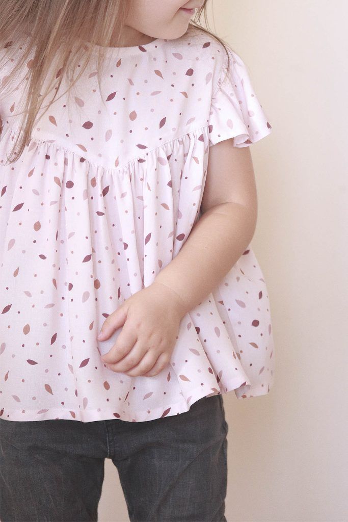 Una niña posa con una blusa rosa con motivos de hojas en tonos rosa oscuro, vino y marrón.