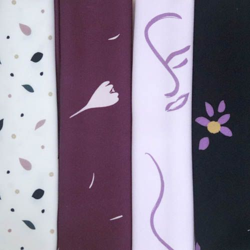 Cuatro muestras de telas. Una tienda fondo blanco con hojas de colores rosas y azules, otra tiene fondo ciruela y tiene motivos de flores, otra es malva con motivos de caras y otra es negra con motivos de margaritas moradas.