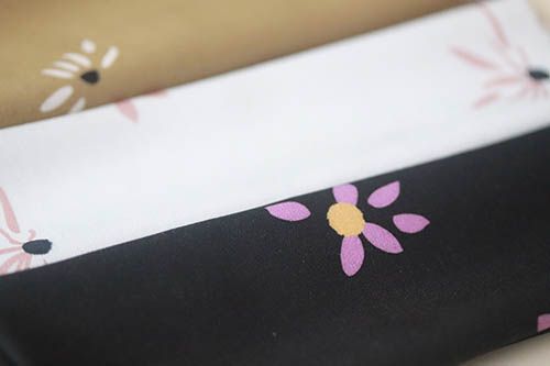 Muestra de tres telas con estampado de margaritas. Una con fondo oliva, otra blanco y otra negro.