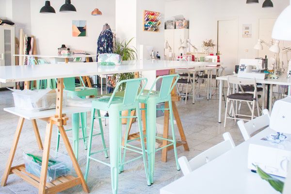 Interior de una academia de costura en la que se ve una mesa alta para cortar telas y hacer patrones. Al fondo se ve una mesa con una máquina de coser.