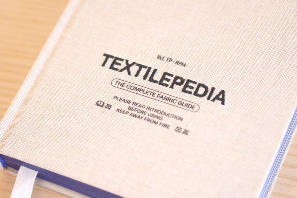 Portada del libro Textilepedia sobre una mesa de madera.