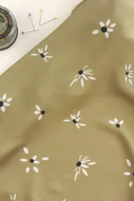 Tela de viscosa color oliva con flores margaritas en color blanco roto y a las que se le están cayendo algunos pétalos.
