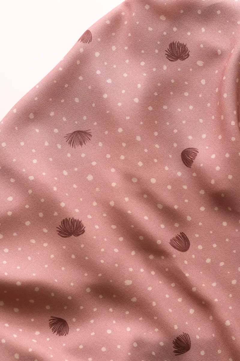 Plano cercano de una viscosa, sobre una mesa, en color rosa arcilloso, con puntitos irregulares en color beige y con flores del árbol de la seda en arcilla oscuro.