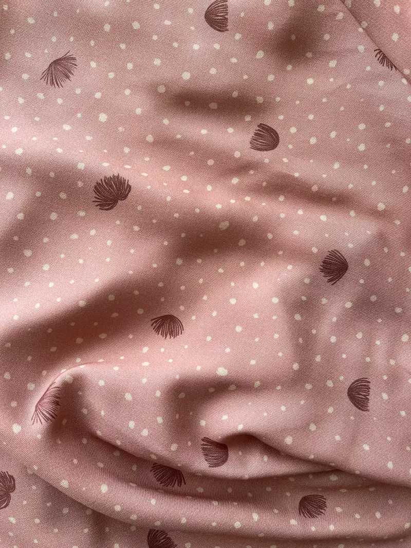 Plano cercano de una viscosa, con partes dobladas para ver el comportamiento de la tela. Es de color rosa arcilloso, con puntitos irregulares en color beige y con flores del árbol de la seda en color arcilla oscuro.