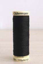 Bobina de hilo Gütermann negro, sobre una madera de color claro y de fondo una pared blanca.