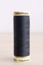 Bobina de hilo Gütermann 095, de color gris oscuro, sobre una madera de color claro y de fondo una pared blanca.