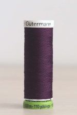 Bobina de hilo Gütermann 135 rPET, de color vino, sobre una madera de color claro y de fondo una pared blanca.