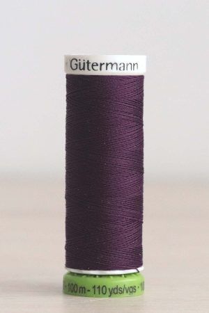 Bobina de hilo Gütermann 135 rPET, de color vino, sobre una madera de color claro y de fondo una pared blanca.