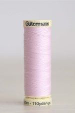 Bobina de hilo Gütermann 372, de color rosa malva, sobre una madera de color claro y de fondo una pared blanca.