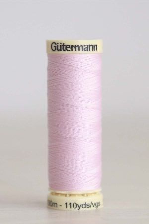 Bobina de hilo Gütermann 372, de color rosa malva, sobre una madera de color claro y de fondo una pared blanca.
