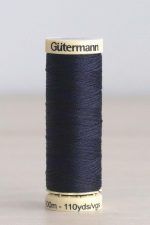 Bobina de hilo Gütermann 387, de color azul oscuro, sobre una madera de color claro y de fondo una pared blanca.