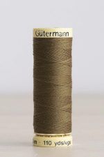 Bobina de hilo Gütermann 528, de color oliva, sobre una madera de color claro y de fondo una pared blanca.
