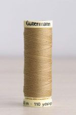 Bobina de hilo Gütermann 591, de color ocre, sobre una madera de color claro y de fondo una pared blanca.