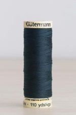 Bobina de hilo Gütermann 596, de color azul verdoso muy oscuro, sobre una madera de color claro y de fondo una pared blanca.