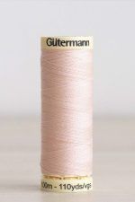 Bobina de hilo Gütermann 658, de color rosa claro, sobre una madera de color claro y de fondo una pared blanca.
