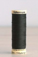 Bobina de hilo Gütermann 687, de color verde muy oscuro, sobre una madera de color claro y de fondo una pared blanca.