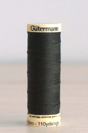 Bobina de hilo Gütermann 687, de color verde muy oscuro, sobre una madera de color claro y de fondo una pared blanca.
