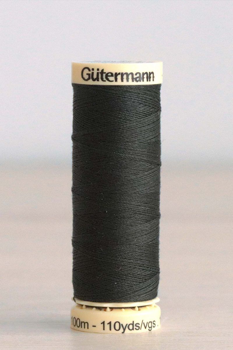 Hilo Gütermann poliéster nº 687 Bobina de hilo Gütermann 687, de color verde muy oscuro, sobre una madera de color claro y de fondo una pared blanca.