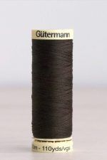 Bobina de hilo Gütermann 697, de color marrón muy oscuro, sobre una madera de color claro y de fondo una pared blanca.