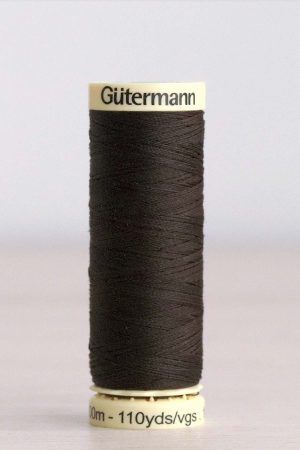 Bobina de hilo Gütermann 697, de color marrón muy oscuro, sobre una madera de color claro y de fondo una pared blanca.