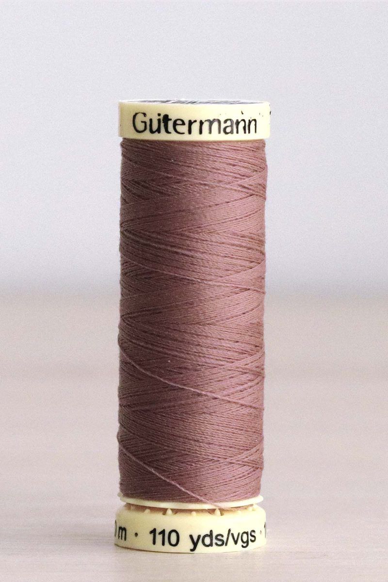 Hilo Gütermann poliéster nº 844 Bobina de hilo Gütermann 844, de color arcilla rosada, sobre una madera de color claro y de fondo una pared blanca.