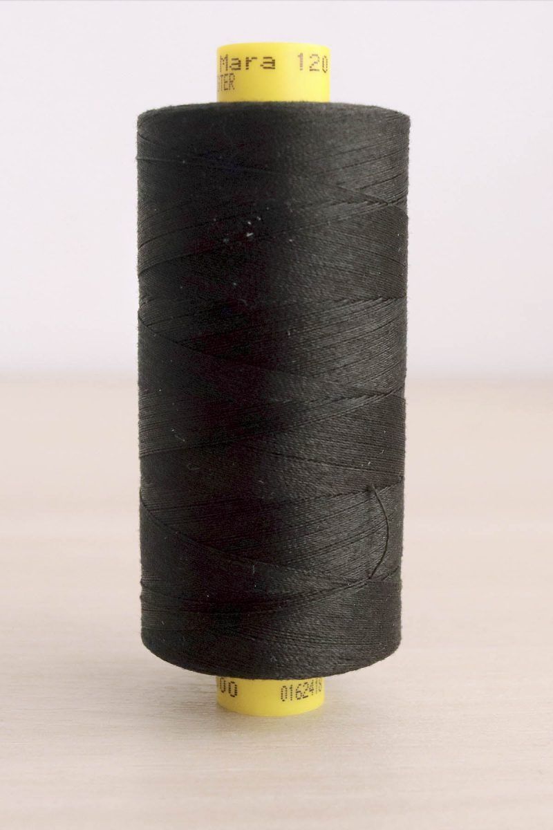 Bobina de hilo Gütermann Mara 120, de color negro, sobre una madera de color claro y de fondo una pared blanca.