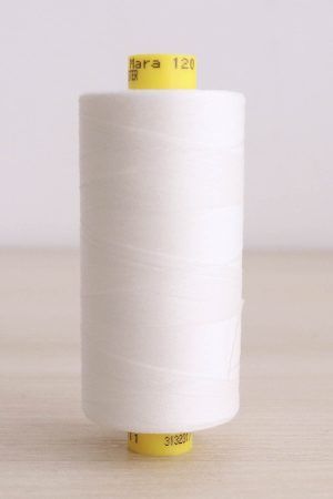 Bobina de hilo Gütermann Mara 120, de color blanco crudo, sobre una madera de color claro y de fondo una pared blanca.