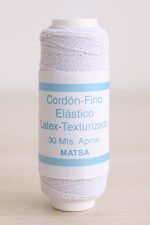 Bobina de hilo elástico para fruncir de color blanco sobre mesa de madera y de fondo una pared blanca.