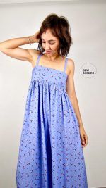 Mujer castaña, de pelo corto, mira hacia abajo y muestra el mono que lleva puesto. Está confeccionado con una tela con mucha caída, de color azul y con estampado de pequeñas flores.