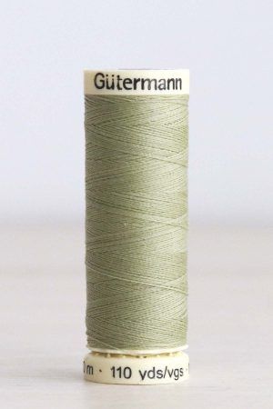 Bobina de hilo Gütermann 282, de color verde, sobre una madera de color claro y de fondo una pared blanca.
