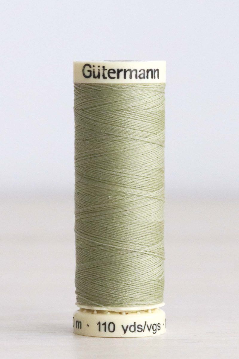 Hilo Gütermann poliéster nº 282 Bobina de hilo Gütermann 282, de color verde, sobre una madera de color claro y de fondo una pared blanca.