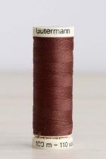 Bobina de hilo Gütermann 478, de color marrón, sobre una madera de color claro y de fondo una pared blanca.