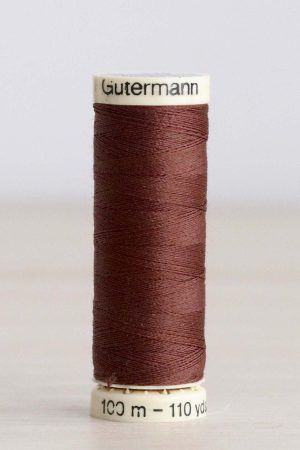Bobina de hilo Gütermann 478, de color marrón, sobre una madera de color claro y de fondo una pared blanca.