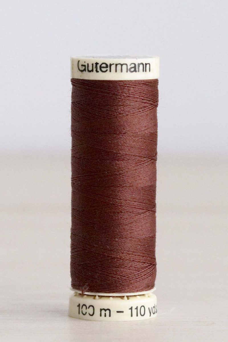 Bobina de hilo Gütermann 478, de color marrón, sobre una madera de color claro y de fondo una pared blanca.