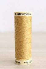 Bobina de hilo Gütermann 488, de color amarillo mostaza, sobre una madera de color claro y de fondo una pared blanca.