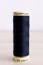 Bobina de hilo Gütermann 711, de color azul oscuro, sobre una madera de color claro y de fondo una pared blanca.