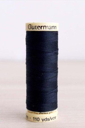 Bobina de hilo Gütermann 711, de color azul oscuro, sobre una madera de color claro y de fondo una pared blanca.