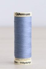 Bobina de hilo Gütermann 72, de color azul claro, sobre una madera de color claro y de fondo una pared blanca.