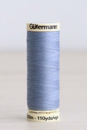 Bobina de hilo Gütermann 72, de color azul claro, sobre una madera de color claro y de fondo una pared blanca.
