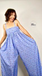 Una mujer castaña, de pelo corto, presume del mono que lleva puesto. Es de tirantes, largo, hecho con una tela con mucha caída, de color azul y con estampado de flores pequeñas.